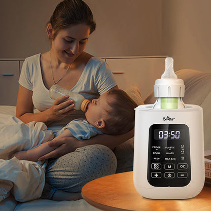 Bear Baby Bottle Warmer on a nightstand for midnight feeding while a mother feeds her baby in the background.