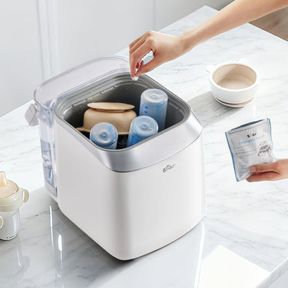 Dropping a Bear Detergent Tablet into a Bottle Washer Pro loaded with baby bottles and feeding gear.