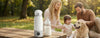 Family and dog relaxing outdoors by a Bear Portable Bottle Warmer for Travel on a picnic table.