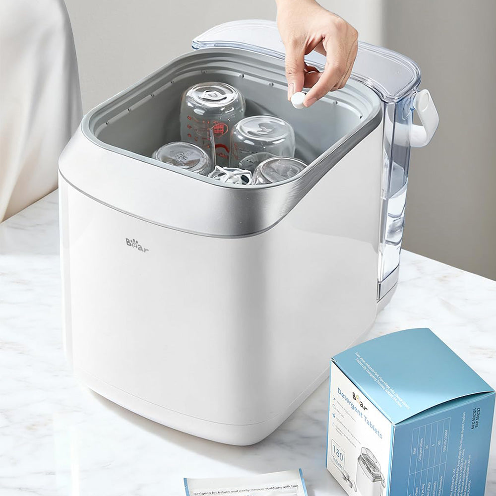 Adding a Bear Detergent Tablet to the Bottle Washer Pro filled with multiple glass baby bottles.