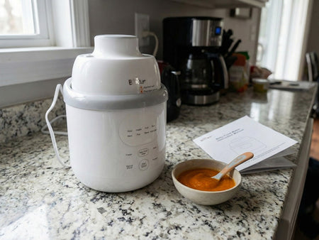 White Bear Baby Food Maker on a granite counter next to an instruction manual and a bowl of orange puree.