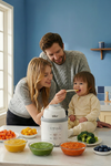 Family feeding baby using the Bear NutriEase Stainless Steel All Stage Baby Food Maker surrounded by colorful fresh purees.