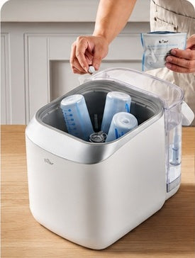 A person adds a detergent tablet after loading bottles and accessories.