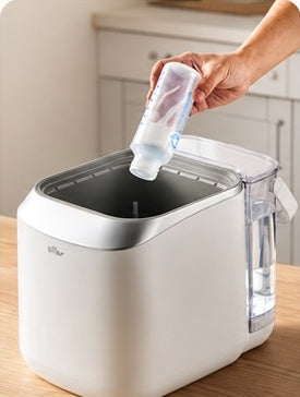 A person places a baby bottle upside down inside the machine.