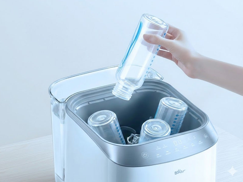 A hand loads an inverted baby bottle into the Bear Bottle Washer Pro.